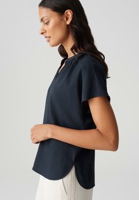 Top a maniche corte blu navy con tessuto texturizzato, scollatura rotonda e orlo curvo. Presenta una vestibilità rilassata e spacchi laterali per il massimo comfort.