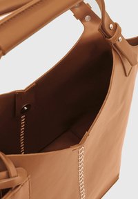 Brun læder tote taske med et minimalistisk design, der har et rummeligt interiør og kontrasterende syninger langs kanterne.