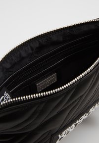 Svart kviltad läderkuvert med dragkedja. Inuti finns flera fack och en logotavla. Silverfärgade detaljer synliga.