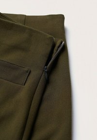 Spodnie z tkaniny w kolorze oliwkowej zieleni, z bocznym zamkiem błyskawicznym i detalem kieszeni. Gładka tekstura z dopasowanym krojem, podkreślająca czyste linie i szwy.