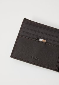 Portafoglio in pelle marrone con più slot per carte e una finitura texture. Il logo del brand è impresso sul frontale.