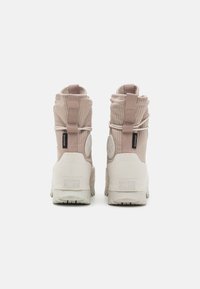 Wysokie sneakersy w jasnym beżu z ryżykowaną tkaniną, gumowymi podeszwami i wyraźnym logo na pięcie. Posiadają podwójne pętle do noszenia.