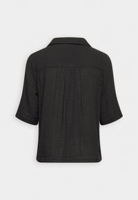 Chemise noire à manches courtes avec un col structuré, présentant un tissu texturé et un détail de plis subtils à l'arrière.