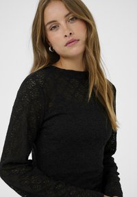 Sort blonde top med lange ærmer, prydet med et blomstertryk. Stoffet har en struktureret overflade, med en rund halsudskæring og tætsiddende design.