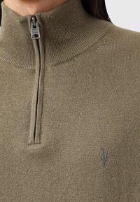 Gebreid olijfgroen sweater met een hoge kraag, voorzien van een halve rits en een klein logo op de borst. Zachte textuur en een getailleerd ontwerp.