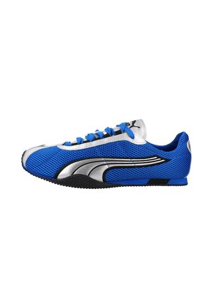 Zapatilla deportiva azul y plateada de perfil bajo con parte superior de malla, logo negro y plateado en el lateral, cordones azules y suela negra texturizada.