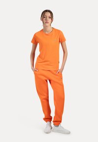 Oranje katoenen T-shirt en bijpassende joggers, met een comfortabele pasvorm, geribde halslijn en elastische manchetten, gecombineerd met witte sneakers.