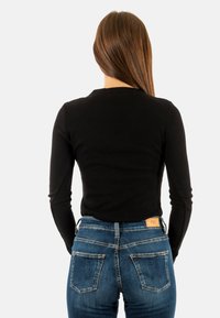 Top à manches longues noir côtelé associé à un jean en denim bleu avec poches arrière et une étiquette en cuir. Design ajusté.