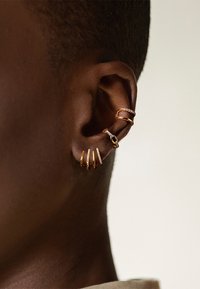 Boucles d'oreilles en ton or avec plusieurs anneaux empilés et un design incurvé et texturé. Quelques accents incluent de petites pierres claires pour le détail.