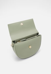 Zelená kožená kabelka s kulatým tvarem a klopovým zavíráním. Obsahuje zlaté kovové detaily, vnitřní přihrádky a hladký povrch.