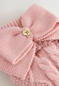 Accessorio lavorato a maglia rosa con un grande fiocco e un bottone dorato a forma di cuore. Presenta una trama a treccia e ulteriori punti decorativi.