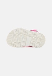 Růžová teniska s bílou gumovou podrážkou. Podešev má horizontální a vertikální drážky pro lepší přilnavost. Velcro pásek pro bezpečné uchycení.