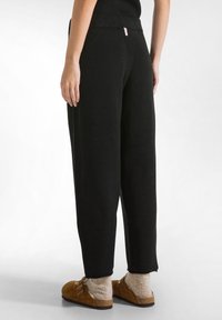 Zwarte, loszittende broek met een zachte textuur en een hoge taille. Voorzien van zijnaadzakken en een klein merklabel op de achterkant.