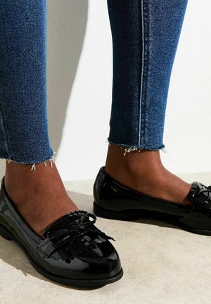 Svarta tåliga läderloafers med frans och rosett. Lågt skuren och rund tå. Kombinerat med slitna jeans i ankellängd.