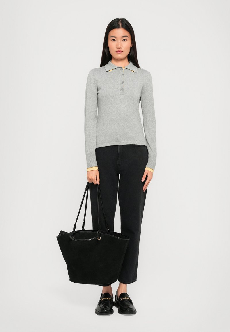 Gray long-sleeve polo with three buttons, yellow collar accents, black high-waisted jeans, and a large black suede tote bag. Black loafers.