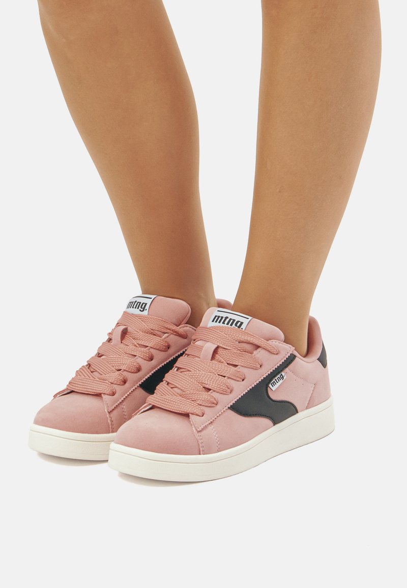 Roze suede sneakers met zwarte accenten, vetersluiting en een witte rubberen zool. Bevat branding op de tong en zijkant.
