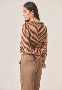 Blusa a rayas marrón y rosa con cuello con volantes, mangas largas abullonadas, cintura ajustada, combinada con pantalones satinados marrones claros con bolsillos.