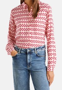 Chemise boutonnée avec un motif en losanges rose et rouge, fabriquée en tissu léger. Associée à un jean en denim bleu taille moyenne. Manches longues et col classique.