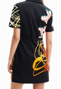 Svart klänning med korta ärmar, en bälte i midjan och livfulla abstrakta mönster i rosa, gult och grönt över ryggen.