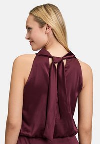 Burgundy satin top featuring a halter neck tied at the back, with a patterned texture and open back design.