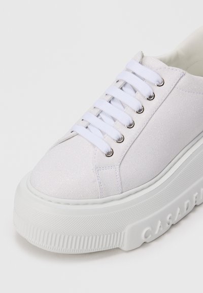 Baltas platform sneakers ar spīdīgu audumu, baltajiem šņorēm, metāla caurumiem un ar "CASADEI" iegravētu biezajā gumijas zole.