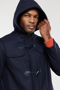 Cappotto blu navy con cappuccio, dotato di ampie tasche a patta, chiusure a toggle e un tessuto testurizzato, con un dettaglio in maglia rossa sui polsini.