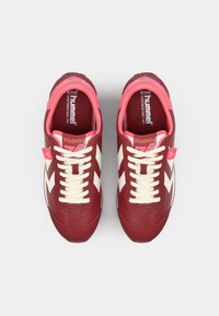 Red and pink athletic shoes with white chevron stripes, textured rubber sole, white laces, and padded collar. Brand label visible inside.