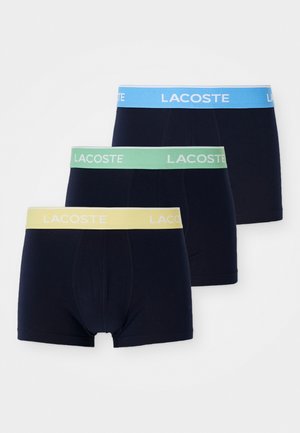 Tres pares de calzoncillos tipo boxers en color navy con cinturillas en contraste: azul, verde y amarillo. Presentan bandas elásticas con el logo "LACOSTE".