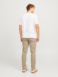 Witte katoenen t-shirt, beige chino's en lichte sneakers gezien vanuit de achterkant. Casual pasvorm, eenvoudig ontwerp, geen zichtbare patronen of logo's.