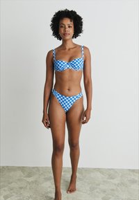 Kék és fehér kockás bikini szett, amely formázott toppal rendelkezik, állítható pántokkal és illeszkedő, magas szabású alsó résszel. Sima szövettextúra.