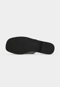 Semelle de chaussure habillée en cuir noir avec un bout carré et un petit talon bloc sur fond clair uni.