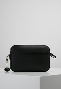 Czarna, prostokątna torba wykonana z teksturowanego materiału. Posiada zamek błyskawiczny oraz dekoracyjny breloczek z okrągłym, ciemnym akcentem.