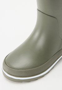 Botte en caoutchouc verte avec une finition lisse, un bout arrondi et une semelle à texture damier. Présente une bande blanche le long du bas.