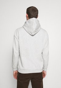 Sudadera gris con una gran capucha ajustable. Fabricada con tejido suave, cuenta con puños y dobladillo acanalados, y un corte relajado. Se muestra la vista trasera.
