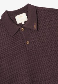 Lilla teksturert polo skjorte med krage, med to brune knapper og et brodert merkenavn på kragen. Størrelse XL.
