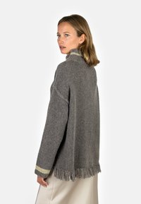 Gray knitted sweater with a high collar, featuring a fringe hem and gold accent stripes on the sleeves. Soft texture and relaxed fit.