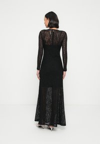 Dolga črna čipkasta obleka z dolgimi rokavi, ki ima oprijeto zgornji del, razširjen krilo in prozoren hrbet. Nežen cvetlični vzorec in zadrga zadaj.