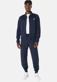 Marineblauw sportief trainingspak met een ritsjack en broek, gemaakt van een textuurstof met subtiele naaddetails en logopersoonlijkheid.
