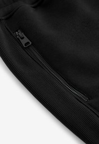 Black athletic pants with a zippered pocket, ribbed cuffs, and smooth fabric texture. Features minimalistic design and sleek stitching detail.