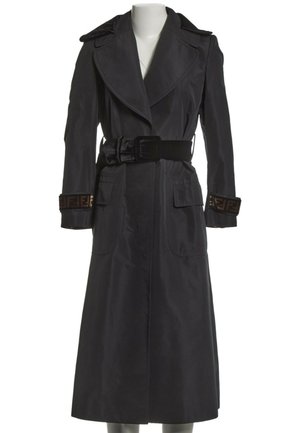Long black trench coat with wide lapels, black belt at the waist, flap pockets, and patterned trim on sleeve cuffs.