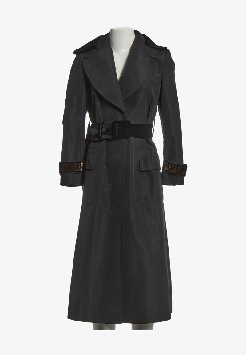 Long trench-coat noir avec larges revers, ceinture noire à la taille, poches à rabat et bordure à motifs aux poignets.