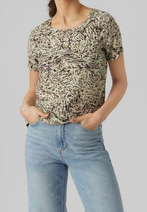 Nainen, jolla on päällään lyhythihainen beige ja ruskea abstraktilla kuviolla varustettu paita, joka on tungettuna korkeavyötäröisiin vaaleansinisiin farkkuihin, kädet taskuissa.