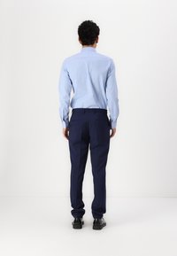 Light blue long-sleeve shirt with button cuffs, paired with dark navy tailored trousers. Worn with black shoes, viewed from the back.