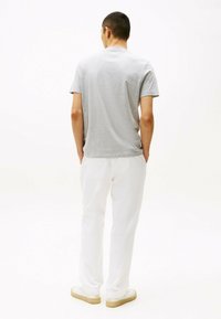 Camiseta gris de manga corta, material de algodón, corte relajado. Pantalones blancos, textura ligera, diseño de pierna recta. Zapatillas blancas con suelas beige.