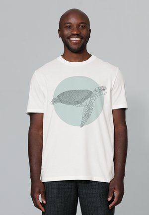Witte T-shirt met korte mouwen, met een afbeelding van een schildpad binnen een zachte groene cirkel, gemaakt van katoen met een gladde textuur.