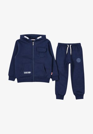 Sweat à capuche pour enfants de couleur bleu marine avec poche avant et fermeture éclair, assorti à un pantalon de survêtement à cordon de serrage arborant un petit logo sur la cuisse.