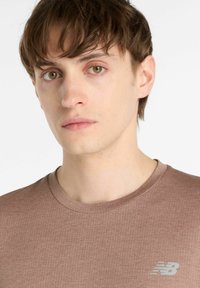 Brown textured New Balance t-shirt with a crew neckline and a small light gray logo on the left chest area.