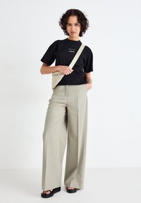Zwarte katoenen t-shirt met wit logo, gecombineerd met lichtbeige wijde broek en zwarte platform sandalen. Inclusief een beige schoudertas.