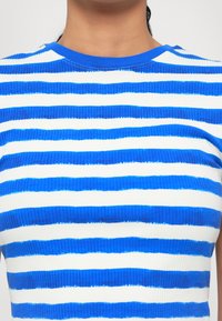 Ribbete topp med veksling mellom tykke blå og hvite striper, rund hals og strukturert stoff.