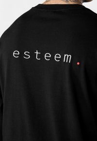 Schwarzes Baumwoll-T-Shirt mit dem Wort "esteem." in weißer Stickerei und einem kleinen roten Punkt als Akzent. Weicher Stoff und lässige Passform.